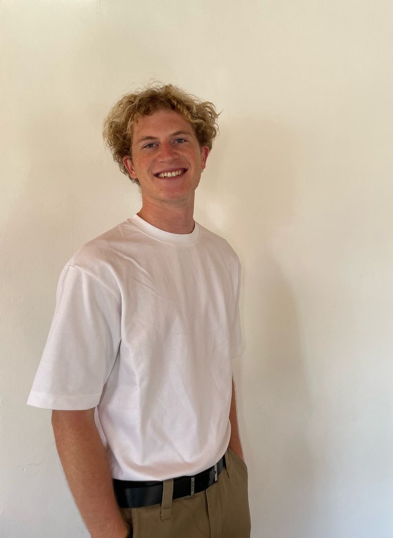 Max Smith smiling in a white t-shirt against a pale wall.
